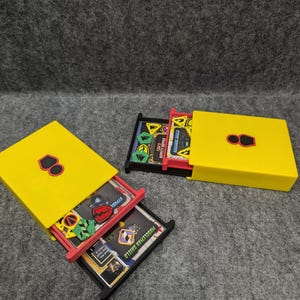 May include: Yellow plastic storage box with a black lid and a red divider. The box is filled with small cards with colorful graphics and text. The text on the cards includes "Musclecar Shield" and "Ryudoll".