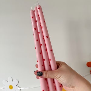 May include: Three pink taper candles with a red heart pattern.