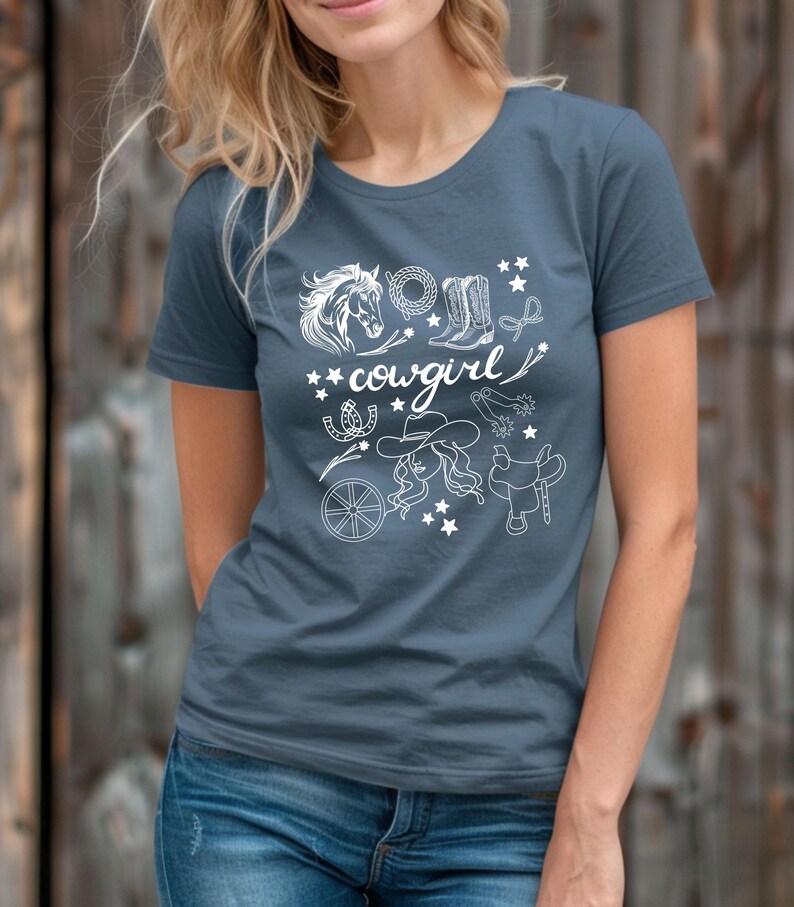 May include: A blue t-shirt with a white design of a horse head, cowboy boots, a horseshoe, a lasso, a saddle, a wagon wheel, and the word 'cowgirl'.