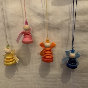 May include: Four handmade angel decorations. Each angel is made from stacked, colourful buttons, with wooden bead heads and ribbon wings. The angels are suspended by strings, displaying a variety of colours including yellow, pink, orange, and blue.