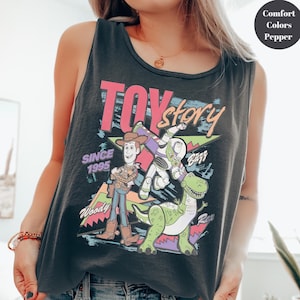 Puede incluir: Una camiseta sin mangas negra con un gr&aacute;fico colorido de los personajes de Toy Story, incluyendo a Woody, Buzz Lightyear y Rex. Tambi&eacute;n se muestra el texto "Toy Story" y "Since 1995". La camiseta sin mangas est&aacute; hecha de un material suave y c&oacute;modo.