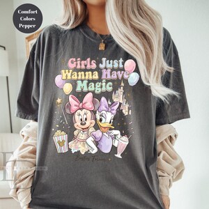 Puede incluir: Camiseta gris oscuro con Minnie Mouse y Daisy Duck y el texto "Girls Just Wanna Have Magic". El dise&ntilde;o incluye globos, un castillo y palomitas de ma&iacute;z. Las palabras "Besties Forever" tambi&eacute;n est&aacute;n impresas en la camiseta.