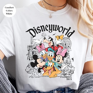 May include: White t-shirt with a black and white graphic of Disney characters, including Mickey Mouse, Minnie Mouse, Donald Duck, and Goofy. The word "Disneyworld" is above the characters, with "Florida 1971" below.