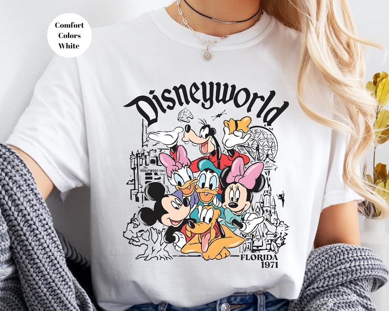May include: White t-shirt with a black and white graphic of Disney characters, including Mickey Mouse, Minnie Mouse, Donald Duck, and Goofy. The word "Disneyworld" is above the characters, with "Florida 1971" below.