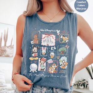 May include: Blue jean tank top featuring a colorful graphic of Disney characters and landmarks. The design includes Mickey Mouse, Donald Duck, and Cinderella's castle. Text on the shirt reads "Walt Disney World" and "The Most Magical Place on Earth."