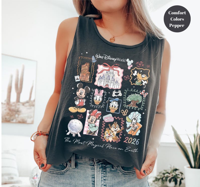 May include: Dark gray tank top featuring a colorful Disney World graphic. The design includes Mickey Mouse, Minnie Mouse, Donald Duck, and other characters, along with the text "Walt Disney World" and "2026". The phrase "The Most Magical Place on Earth" is also printed on the shirt.