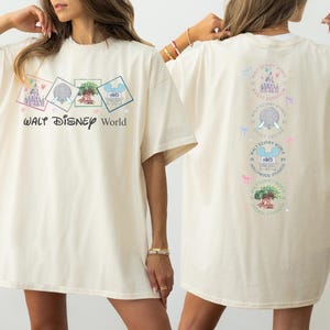 May include: Cream-colored t-shirt featuring the text "Walt Disney World" with four square graphics of Disney park icons. The back of the shirt displays the same icons in a vertical row, with the park names and logos.