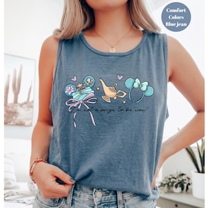 May include: Blue jean tank top with a whimsical graphic featuring a genie lamp, mouse ears, and a gift box. The text "I'm not a prize to be won!" is printed below the graphic. The tank top is a comfort color.