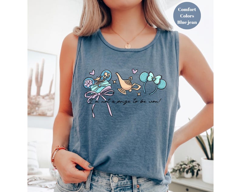 May include: Blue jean tank top with a whimsical graphic featuring a genie lamp, mouse ears, and a gift box. The text "I'm not a prize to be won!" is printed below the graphic. The tank top is a comfort color.