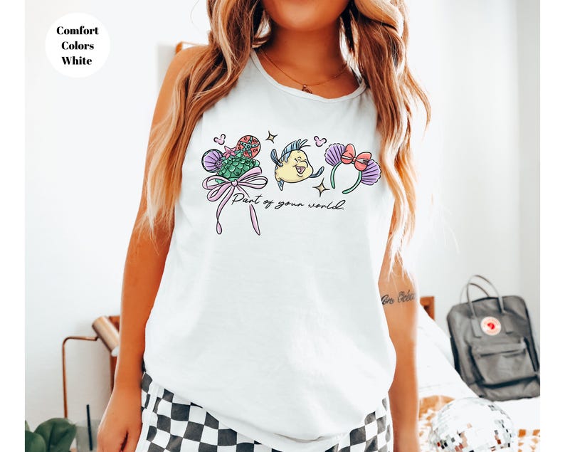 May include: White tank top featuring a colorful graphic design with the text "Part of your world." The design includes cartoon illustrations of a mermaid, a fish, and floral elements. The top is labeled "Comfort Colors White."