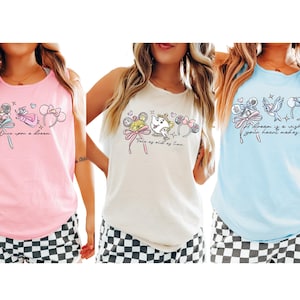 May include: Three tank tops in pink, cream, and light blue, each featuring a different Disney-themed graphic. The pink top has the text "Once upon a dream." The cream top says "Tale as old as time." The blue top reads "A dream is a wish your heart makes."