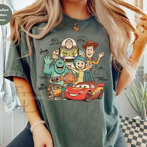 Puede incluir: Una camiseta de manga corta color verde musgo con un estampado gr&aacute;fico de varios personajes animados, incluidos Buzz Lightyear, Sulley, Woody, Joy, Nemo, Wall-E y Lightning McQueen, con sus nombres escritos en letra negra alrededor.