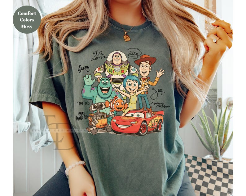 Puede incluir: Una camiseta de manga corta color verde musgo con un estampado gr&aacute;fico de varios personajes animados, incluidos Buzz Lightyear, Sulley, Woody, Joy, Nemo, Wall-E y Lightning McQueen, con sus nombres escritos en letra negra alrededor.