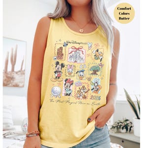 May include: Yellow tank top with a colorful Disney World graphic. The graphic features various Disney characters and landmarks, with the text "Walt Disney World" and "The Most Magical Place on Earth". The year "2026" is also displayed.