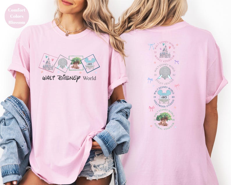 May include: Pink t-shirt with "Walt Disney World" text and four square graphics featuring Disney park icons. The back of the shirt displays additional Disney World graphics and text. The shirt has rolled-up sleeves.