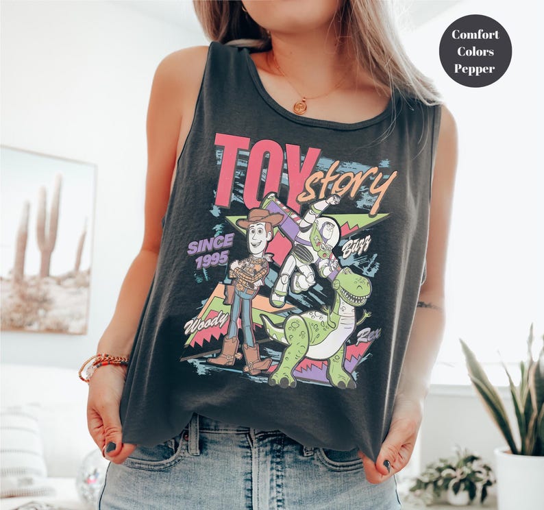 Puede incluir: Una camiseta sin mangas negra con un gr&aacute;fico colorido de los personajes de Toy Story, incluyendo a Woody, Buzz Lightyear y Rex. Tambi&eacute;n se muestra el texto "Toy Story" y "Since 1995". La camiseta sin mangas est&aacute; hecha de un material suave y c&oacute;modo.