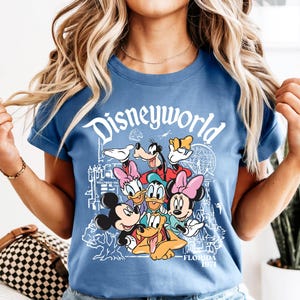 May include: A blue t-shirt with the word "Disneyworld" in white script and a graphic of Disney characters such as Mickey and Minnie Mouse, Donald Duck, and Goofy. The shirt also has the text "Florida 1971".