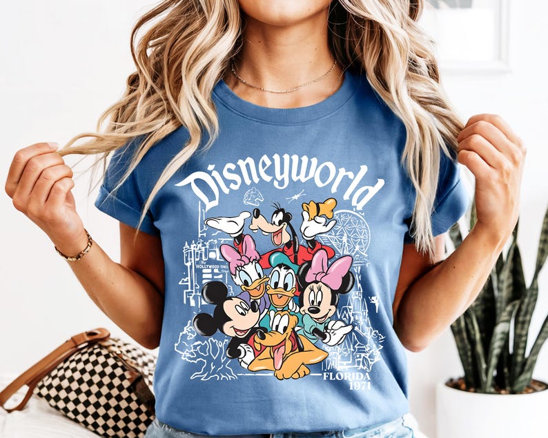 May include: A blue t-shirt with the word "Disneyworld" in white script and a graphic of Disney characters such as Mickey and Minnie Mouse, Donald Duck, and Goofy. The shirt also has the text "Florida 1971".