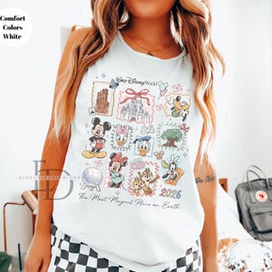 May include: White tank top featuring a colorful Disney World graphic. The design includes various Disney characters and landmarks, with the text "Walt Disney World" and "The Most Magical Place on Earth". The year "2026" is also displayed.