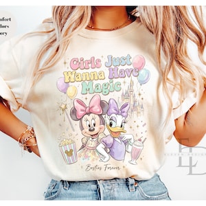 Puede incluir: Camiseta color marfil con Minnie Mouse y Daisy Duck, texto "Girls Just Wanna Have Magic" y "Besties Forever". El dise&ntilde;o incluye un castillo, globos, palomitas de ma&iacute;z y un batido. La camiseta es de color confort.