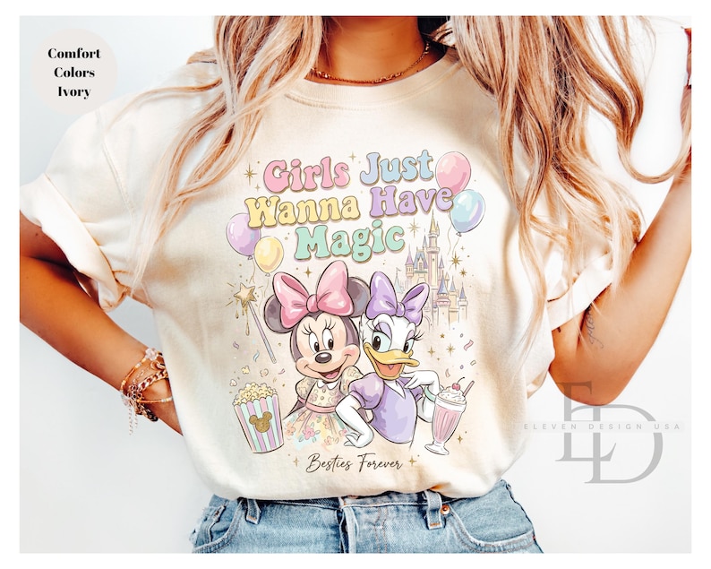 Puede incluir: Camiseta color marfil con Minnie Mouse y Daisy Duck, texto "Girls Just Wanna Have Magic" y "Besties Forever". El dise&ntilde;o incluye un castillo, globos, palomitas de ma&iacute;z y un batido. La camiseta es de color confort.