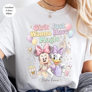 Puede incluir: Camiseta blanca con Minnie Mouse y Daisy Duck con el texto "Girls Just Wanna Have Magic". El dise&ntilde;o incluye un castillo, globos, palomitas de ma&iacute;z y un batido. Tambi&eacute;n est&aacute;n presentes las palabras "Besties Forever".