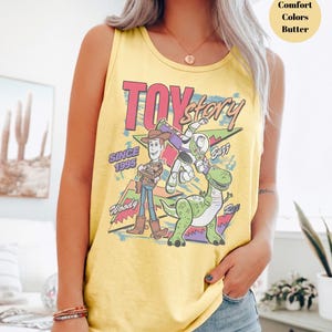 Puede incluir: Camiseta sin mangas amarilla con un gr&aacute;fico de los personajes de Toy Story Woody, Buzz Lightyear y Rex. Las palabras "Toy Story" y "Since 1995" est&aacute;n impresas en la parte delantera. La camiseta sin mangas es de color confort y color mantequilla.
