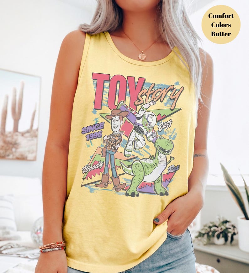 Puede incluir: Camiseta sin mangas amarilla con un gr&aacute;fico de los personajes de Toy Story Woody, Buzz Lightyear y Rex. Las palabras "Toy Story" y "Since 1995" est&aacute;n impresas en la parte delantera. La camiseta sin mangas es de color confort y color mantequilla.