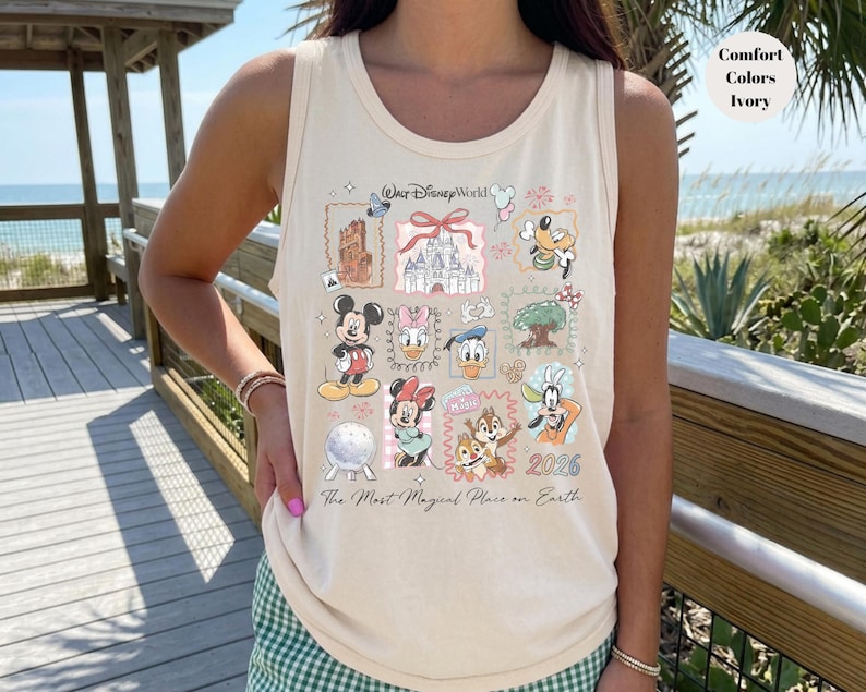 May include: Ivory-colored tank top featuring a colorful collage of Disney World imagery. The design includes Mickey Mouse, Minnie Mouse, Donald Duck, and other characters, along with the text "Walt Disney World" and "2026". The phrase "The Most Magical Place on Earth" is also printed on the shirt.