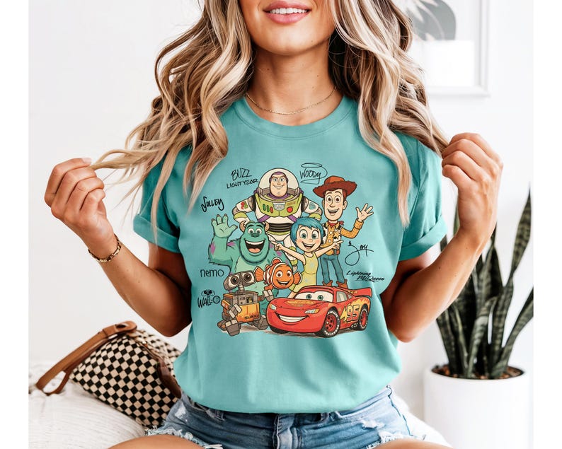 Puede incluir: Una camiseta de manga corta color verde azulado con un estampado gr&aacute;fico de varios personajes animados, incluyendo a Buzz Lightyear, Woody, Sulley, Joy, Nemo, Wall-E y Lightning McQueen, con sus nombres escritos en una fuente cursiva estilizada.