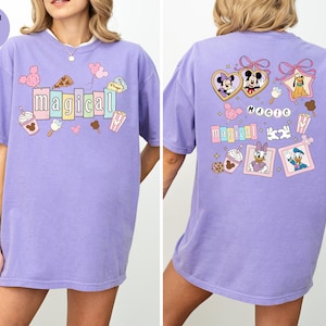 Op de afbeelding: Een lila T-shirt met het woord "magical" in kleurrijke blokletters op de voorkant. Het shirt heeft cartoonafbeeldingen van Mickey Mouse, Minnie Mouse en andere Disney-personages. De achterkant van het shirt heeft het woord "magic" en meer Disney-personageafbeeldingen.