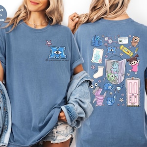 May include: Blue jean colored t-shirt featuring a cartoon design from the movie Monsters, Inc. The front has a blue letter "M" with an eye and the text "We scare because we care!". The back has various cartoon characters and objects.
