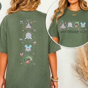 May include: Moss green t-shirt with a Walt Disney World graphic. The front features the text "Walt Disney World" and four small illustrations. The back has a vertical design with castle, Spaceship Earth, Mickey Mouse, and Animal Kingdom graphics.