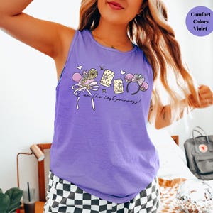 May include: A violet tank top with a graphic that includes a bow, candy, and mouse ears. The text "I am the lost princess!" is printed on the front. The words "Comfort Colors Violet" are in a circle in the upper right corner.