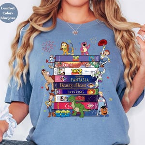 May include: Blue jean-colored t-shirt featuring a stack of VHS tapes with Disney movie titles and characters from Toy Story, Bambi, and Beauty and the Beast. The shirt has the words "Comfort Colors" and "Blue jean" printed on it.