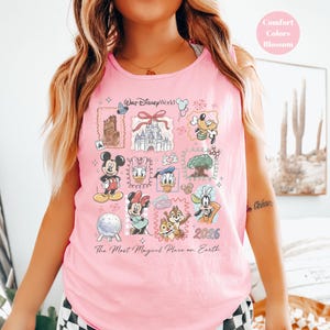 May include: Pink tank top featuring a colorful graphic of Disney characters and landmarks. The design includes Mickey Mouse, Donald Duck, and Cinderella's castle. Text on the shirt reads "Walt Disney World" and "The Most Magical Place on Earth."