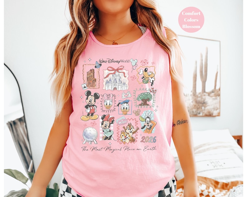 May include: Pink tank top featuring a colorful graphic of Disney characters and landmarks. The design includes Mickey Mouse, Donald Duck, and Cinderella's castle. Text on the shirt reads "Walt Disney World" and "The Most Magical Place on Earth."