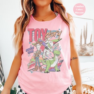 Puede incluir: Camiseta sin mangas rosa con un gr&aacute;fico de Toy Story con Woody, Buzz Lightyear y Rex. Tambi&eacute;n se muestra el texto "Toy Story" y "Since 1995". La camiseta sin mangas es de color Blossom.