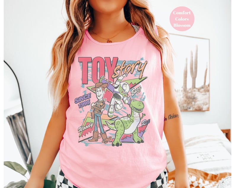 Puede incluir: Camiseta sin mangas rosa con un gr&aacute;fico de Toy Story con Woody, Buzz Lightyear y Rex. Tambi&eacute;n se muestra el texto "Toy Story" y "Since 1995". La camiseta sin mangas es de color Blossom.