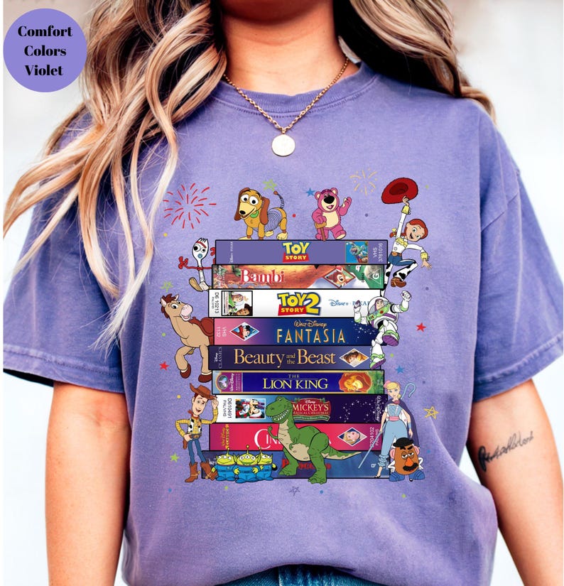 May include: A violet-colored t-shirt featuring a stack of Disney VHS tapes with characters from Toy Story, Bambi, Fantasia, Beauty and the Beast, The Lion King, and more. The shirt also has the text "Comfort Colors Violet".