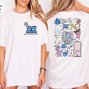 May include: White t-shirt featuring a cartoon design from the movie Monsters, Inc. The front has a blue "M" with an eye and the text "We scare because we care!" The back has various cartoon characters and objects.