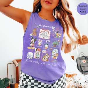 May include: A sleeveless purple tank top featuring a colorful graphic design with Disney characters and landmarks. The design includes Mickey Mouse, Minnie Mouse, Donald Duck, and Chip and Dale. Text on the shirt reads "Walt Disney World" and "The Most Magical Place on Earth 2026."