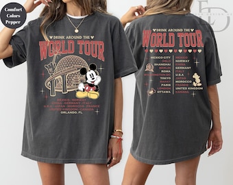 May include: Dark gray t-shirt featuring a graphic of Mickey Mouse in front of a stylized globe with the text "Drink Around The World Tour". The back of the shirt lists various cities. The shirt is a comfort colors pepper.