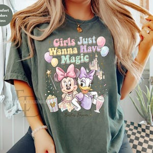 Puede incluir: Camiseta verde oscuro con el texto "Girls Just Wanna Have Magic" e ilustraciones de Minnie Mouse, Daisy Duck, un castillo y globos. La camiseta tambi&eacute;n presenta palomitas de ma&iacute;z y un batido.