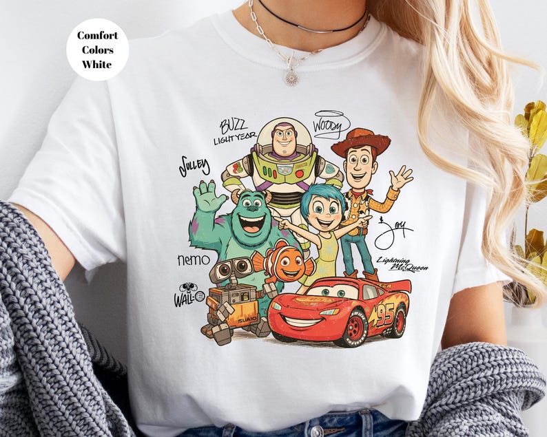 Puede incluir: Una camiseta blanca con un estampado gr&aacute;fico de varios personajes animados, incluidos Buzz Lightyear, Woody, Sulley, Joy, Nemo, Wall-E y Lightning McQueen, con sus nombres escritos en una fuente manuscrita estilizada junto a cada personaje.