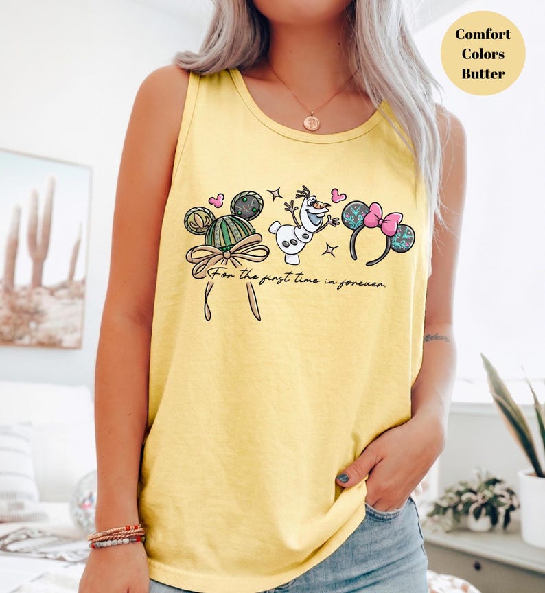 May include: Yellow tank top with a Disney-themed graphic. The design includes Mickey Mouse ears, Olaf the snowman, and the phrase "For the first time in forever." The top is a comfort color in butter yellow.