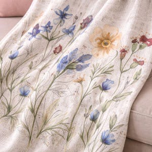 May include: A cream-coloured textile with a watercolour floral design. The pattern includes blue, yellow, and red flowers with green stems and leaves. The fabric has a textured appearance, suggesting a linen or similar material.