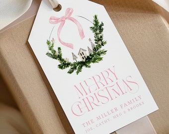May include: White gift tag with a pink bow and a watercolor wreath of green pine branches, white stars, and small houses. The text "Merry Christmas" is in pink lettering and below it reads "The Miller Family Joe, Cathy, Meg & Brooks".