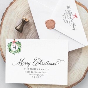 May include: A festive stationery set with a white card inscribed with "Merry Christmas" in cursive, a wreath with the letter "H", and an envelope with "The Harrington Family" printed on it. A wax seal and a sealing stamp are also present.