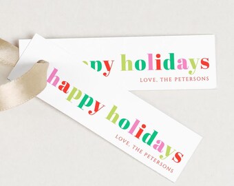 May include: Two white rectangular gift tags with the text "happy holidays" in colorful letters. The tags also include the text "LOVE, THE PETERSONS" in a smaller font. A beige ribbon is attached to one tag.
